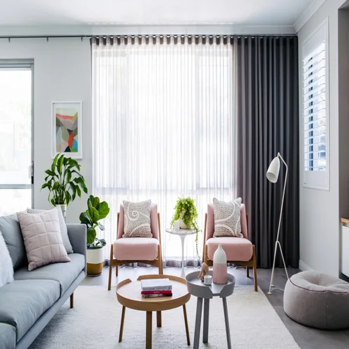 Modern living room with gray curtains and sheer white drapes, a gray sofa, and pink accent chairs